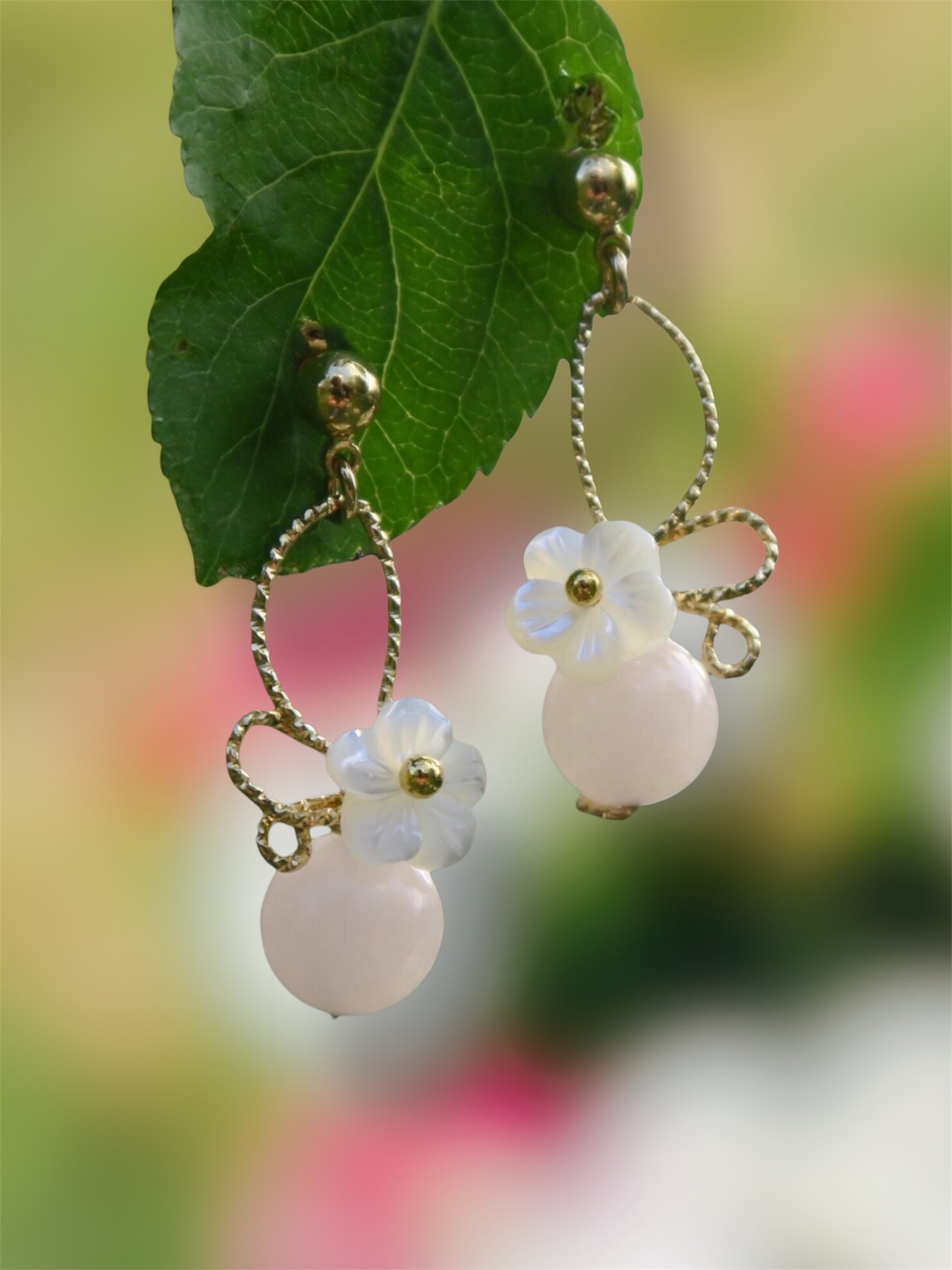 paire de boucles d'oreilles rose dorées et blanche dans le jardin