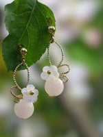 paire de boucles d'oreilles rose dorées et blanche dans le jardin