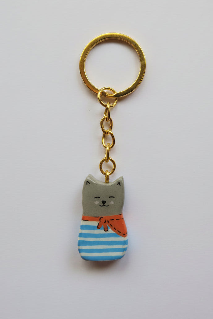 Porte-clé Lucky Rolie Cat Eddy — petit chat gris breton espiègle en marinière, modelé et peint à la main en argile, fini à la résine UV. Pièce unique fait main en Bretagne.