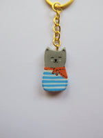 Porte-clé Lucky Rolie Cat Eddy — petit chat gris breton espiègle en marinière, modelé et peint à la main en argile, fini à la résine UV. Pièce unique fait main en Bretagne.