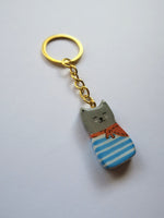 Porte-clé Lucky Rolie Cat Eddy — petit chat gris breton espiègle en marinière, modelé et peint à la main en argile, fini à la résine UV. Pièce unique fait main en Bretagne.
