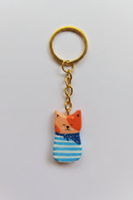 Porte-clé Lucky Rolie Cat Émile — petit chat roux breton malicieux en marinière, modelé et peint à la main en argile, fini à la résine UV. Pièce unique fait main en Bretagne.