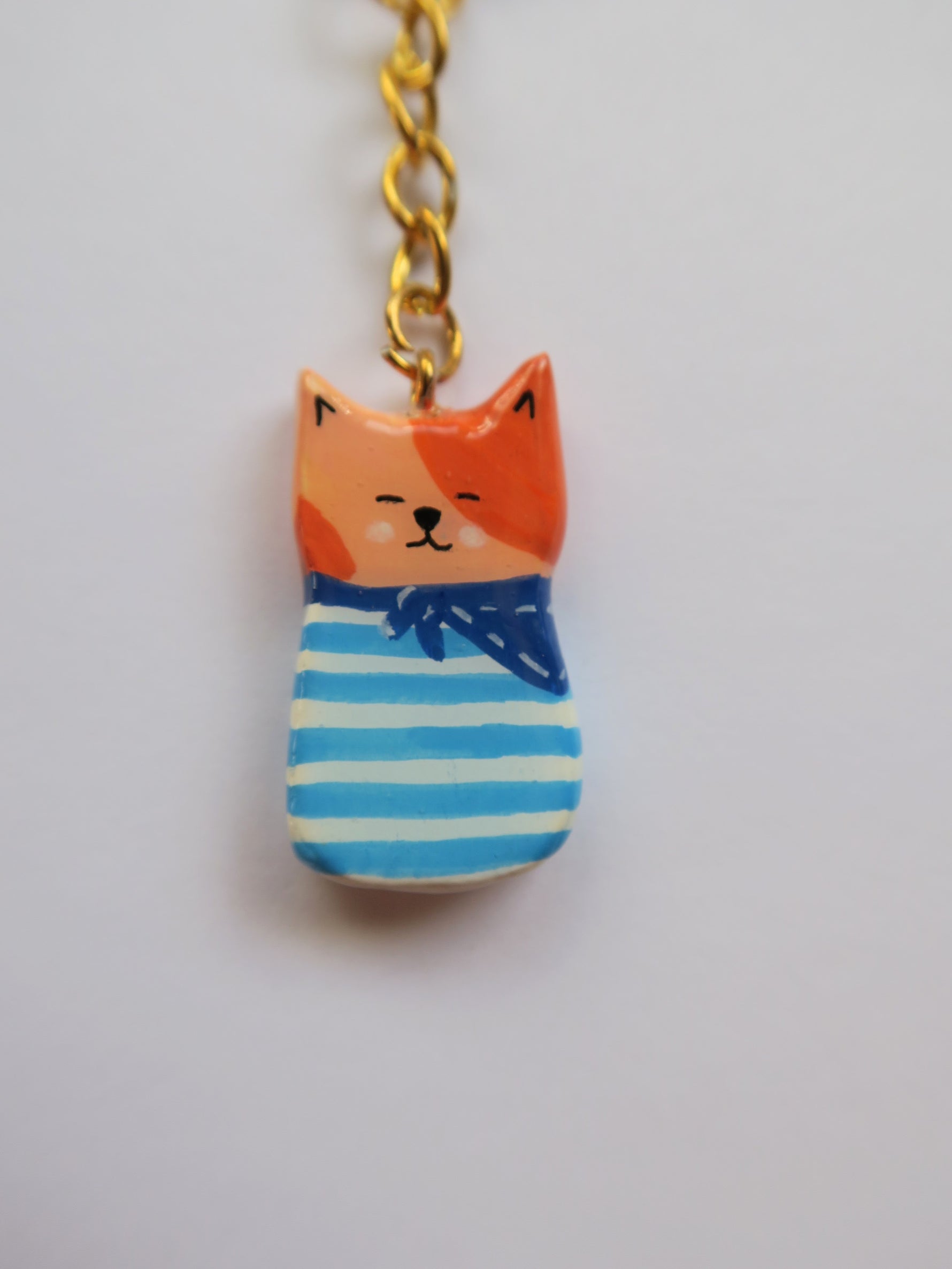 Porte-clé Lucky Rolie Cat Émile — petit chat roux breton malicieux en marinière, modelé et peint à la main en argile, fini à la résine UV. Pièce unique fait main en Bretagne.