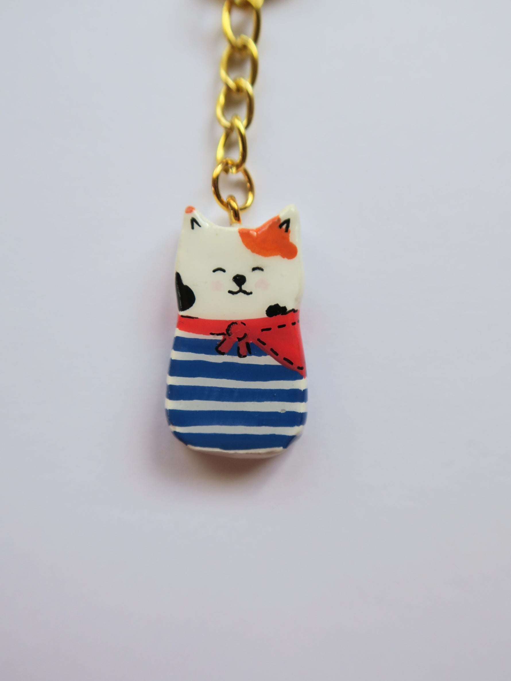 Porte-clé Lucky Rolie Cat Gwendal — petit chat tricolore breton en marinière bleu marine, modelé et peint à la main en argile, fini à la résine UV. Pièce unique fait main en Bretagne.