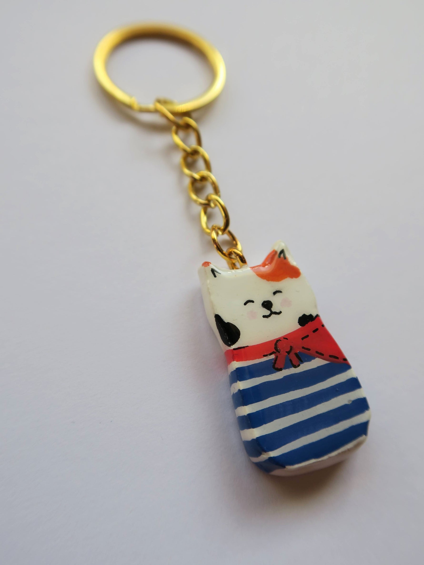 Porte-clé Lucky Rolie Cat Gwendal — petit chat tricolore breton en marinière bleu marine, modelé et peint à la main en argile, fini à la résine UV. Pièce unique fait main en Bretagne.