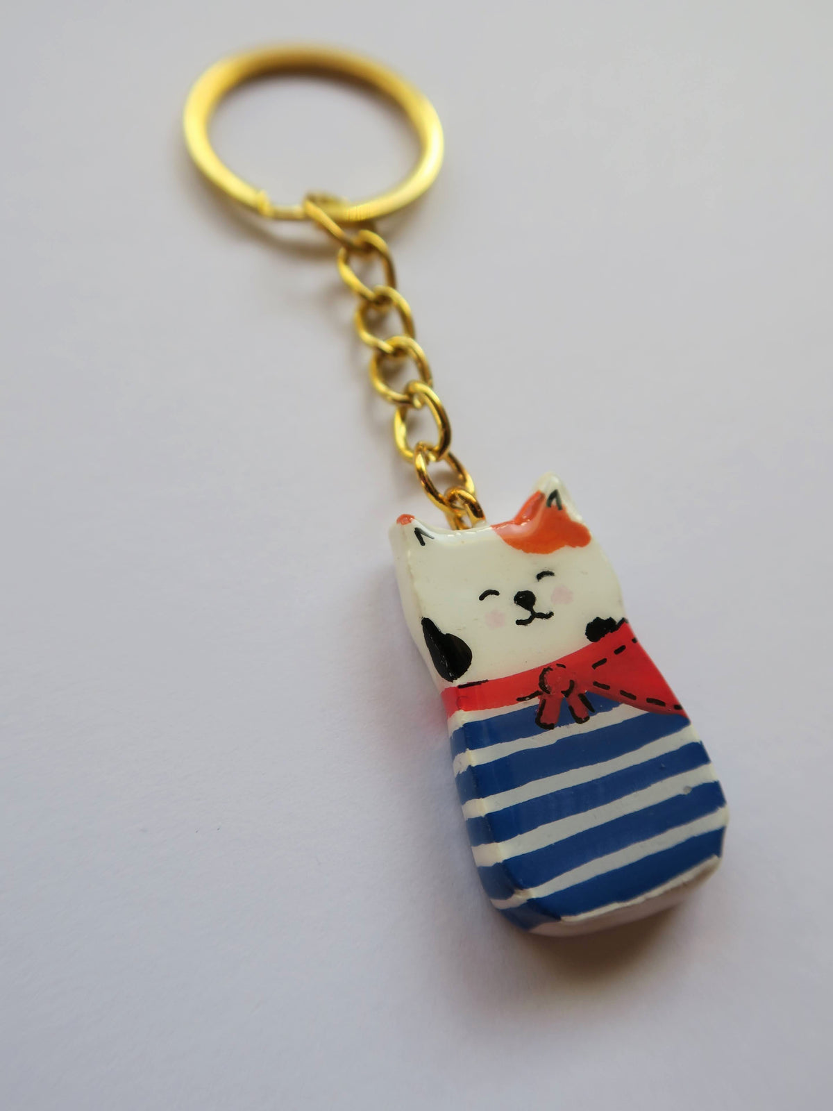 Porte-clé Lucky Rolie Cat Gwendal — petit chat tricolore breton en marinière bleu marine, modelé et peint à la main en argile, fini à la résine UV. Pièce unique fait main en Bretagne.