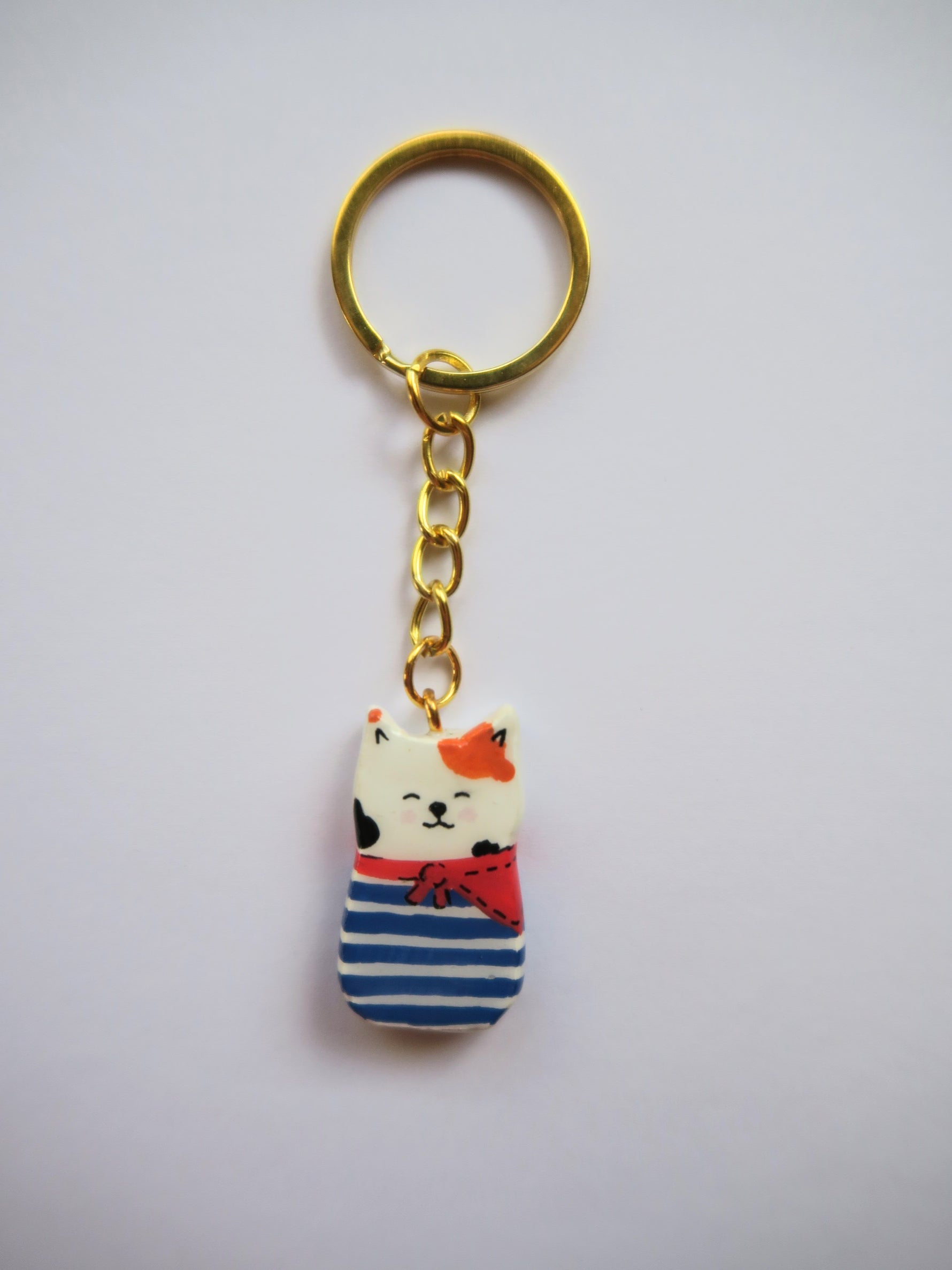 Porte-clé Lucky Rolie Cat Gwendal — petit chat tricolore breton en marinière bleu marine, modelé et peint à la main en argile, fini à la résine UV. Pièce unique fait main en Bretagne.