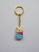 Porte-clé Lucky Rolie Cat Loïc — petit chat blanc breton joyeux en marinière, modelé et peint à la main en argile, fini à la résine UV. Pièce unique fait main en Bretagne.
