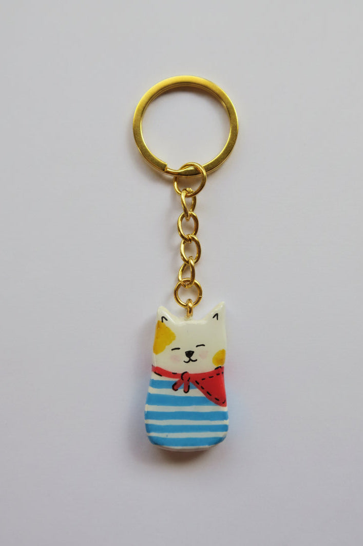 Porte-clé Lucky Rolie Cat Loïc — petit chat blanc breton joyeux en marinière, modelé et peint à la main en argile, fini à la résine UV. Pièce unique fait main en Bretagne.