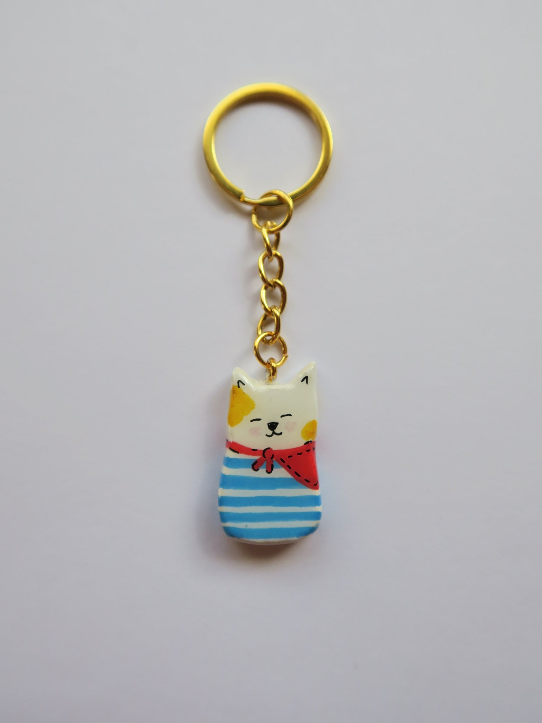 Porte-clé Lucky Rolie Cat Loïc — petit chat blanc breton joyeux en marinière, modelé et peint à la main en argile, fini à la résine UV. Pièce unique fait main en Bretagne.