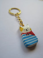 Porte-clé Lucky Rolie Cat Loïc — petit chat blanc breton joyeux en marinière, modelé et peint à la main en argile, fini à la résine UV. Pièce unique fait main en Bretagne.