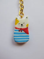 Porte-clé Lucky Rolie Cat Loïc — petit chat blanc breton joyeux en marinière, modelé et peint à la main en argile, fini à la résine UV. Pièce unique fait main en Bretagne.