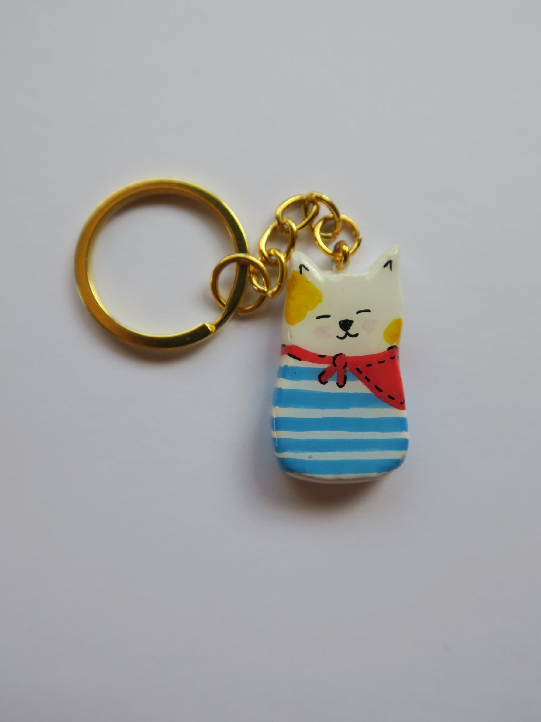 Porte-clé Lucky Rolie Cat Loïc — petit chat blanc breton joyeux en marinière, modelé et peint à la main en argile, fini à la résine UV. Pièce unique fait main en Bretagne.