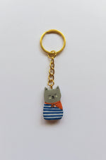Porte-clé Lucky Rolie Cat Martin — petit chat gris breton en marinière, modelé et peint à la main en argile, fini à la résine UV. Pièce unique fait main en Bretagne.