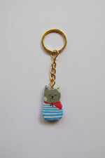 Porte-clé Lucky Rolie Cat Paul — petit chat gris breton en marinière, modelé et peint à la main en argile, fini à la résine UV. Pièce unique fait main en Bretagne.