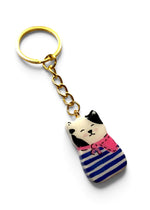 Porte-clé Lucky Rolie Cat Erwan petit chat breton noir et blanc en marinière bleue et foulard rose, modelé et peint à la main en argile, fini à la résine UV. Livré dans son emballage cadeau. Fait main au Cap Sizun.