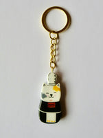 Porte-clé Lucky Rolie Cat Nolwenn — chatte bigoudène blanche tachetée en costume traditionnel, modelée et peinte en argile, finie à la résine UV. Fait main au Cap Sizun.