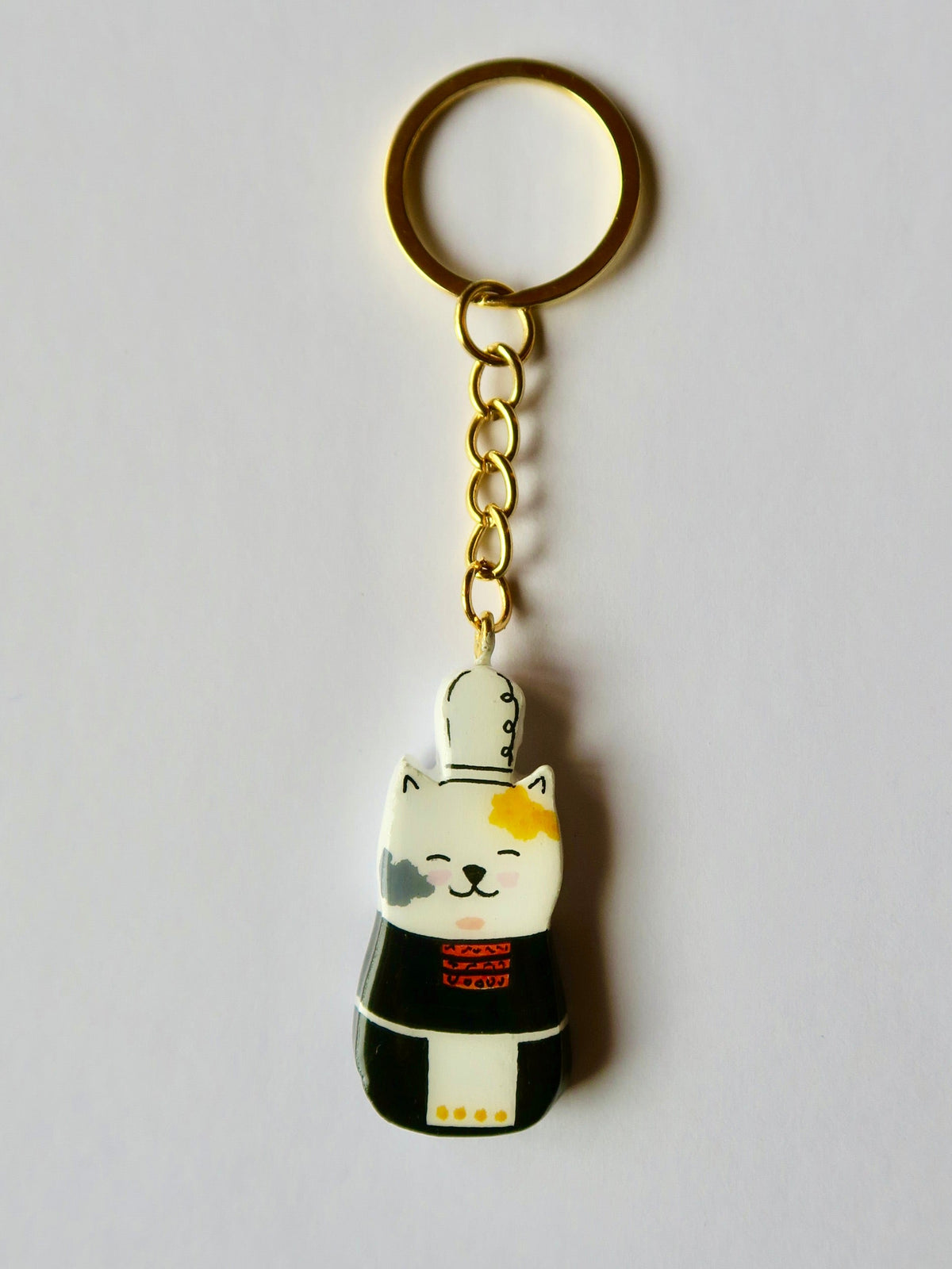 Porte-clé Lucky Rolie Cat Nolwenn — chatte bigoudène blanche tachetée en costume traditionnel, modelée et peinte en argile, finie à la résine UV. Fait main au Cap Sizun.