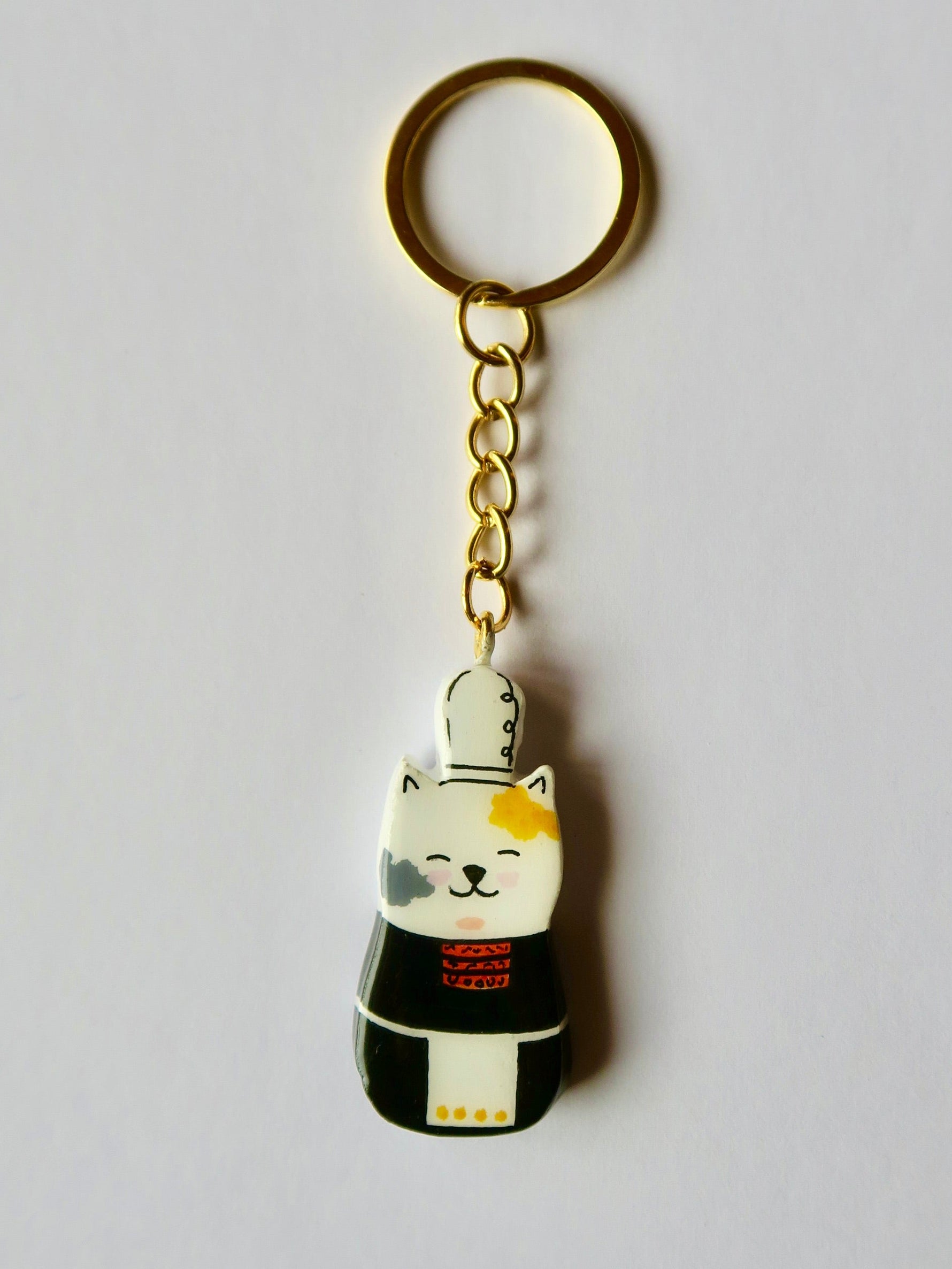 Porte-clé Lucky Rolie Cat Nolwenn — chatte bigoudène blanche tachetée en costume traditionnel, modelée et peinte en argile, finie à la résine UV. Fait main au Cap Sizun.