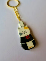 Porte-clé Lucky Rolie Cat Nolwenn — chatte bigoudène blanche tachetée en costume traditionnel, modelée et peinte en argile, finie à la résine UV. Fait main au Cap Sizun.