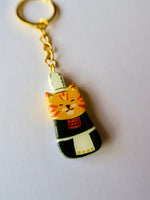 Porte-clé Lucky Rolie Cat Soizic — chatte bigoudène rousse en costume traditionnel, modelée et peinte à la main en argile, finie à la résine UV. Fait main au Cap Sizun.