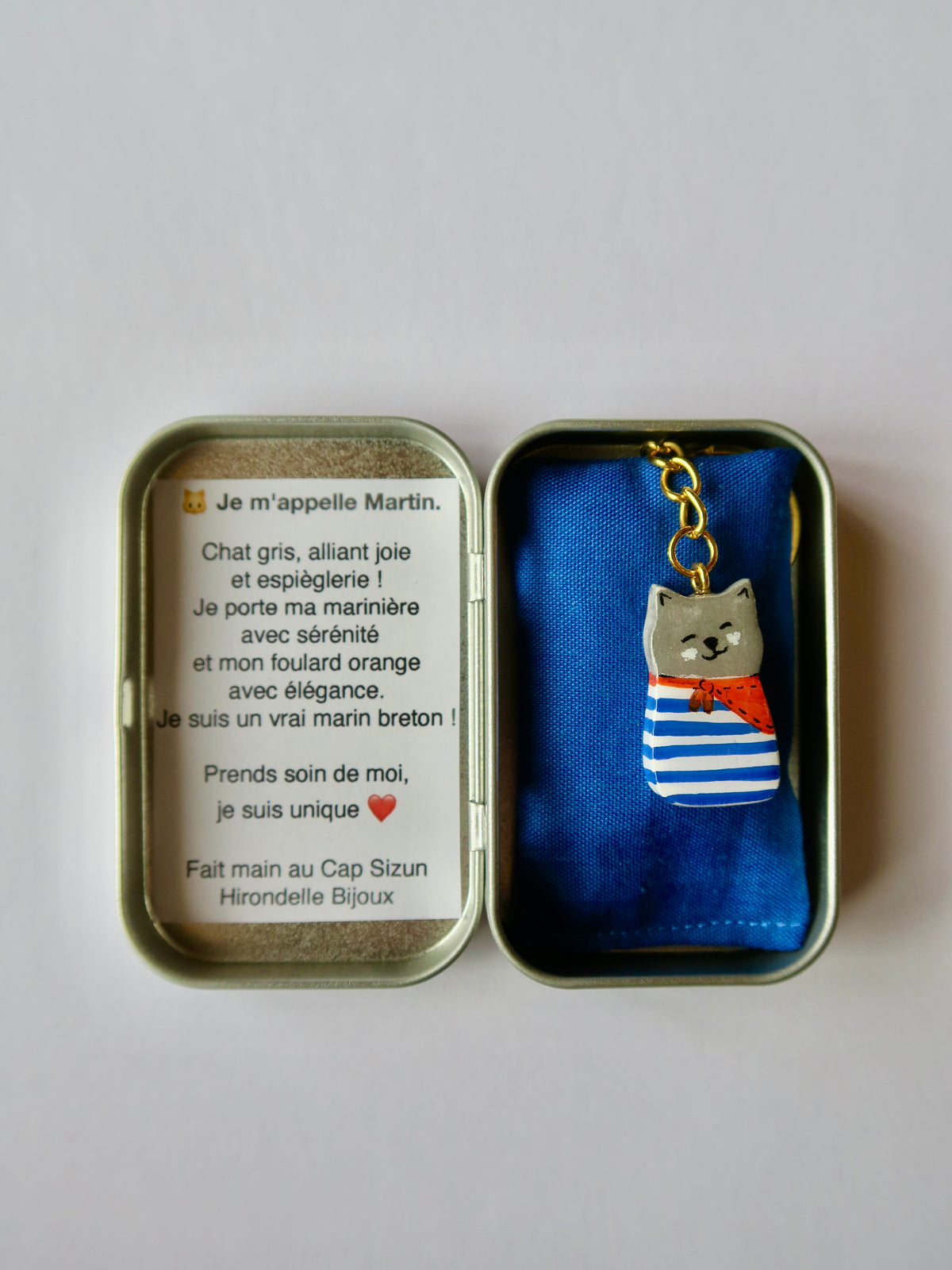Porte-clé Lucky Rolie Cat martin — petit chat gris breton en marinière rose pastel et foulard bleu, modelé et peint à la main en argile, fini à la résine UV. Fait main au Cap Sizun.