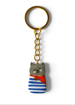 Porte-clé Lucky Rolie Cat Martin — petit chat gris breton en marinière, modelé et peint à la main en argile, fini à la résine UV. Pièce unique fait main en Bretagne.