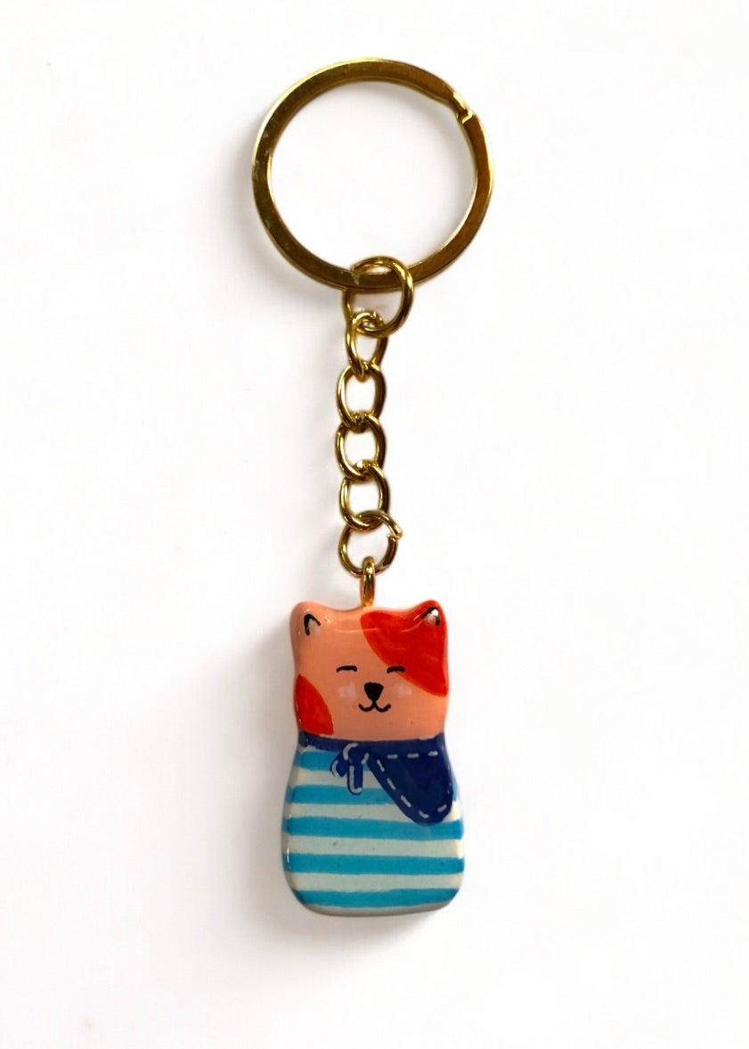 Porte-clé Lucky Rolie Cat Émile — petit chat roux breton malicieux en marinière, modelé et peint à la main en argile, fini à la résine UV. Pièce unique fait main en Bretagne.