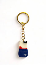Porte-clé Lucky Rolie Cat Gwendal — petit chat tricolore breton en marinière bleu marine, modelé et peint à la main en argile, fini à la résine UV. Pièce unique fait main en Bretagne.