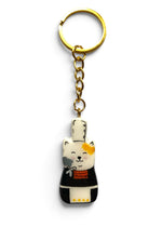 Porte-clé Lucky Rolie Cat Nolwenn — chatte bigoudène blanche tachetée en costume traditionnel, modelée et peinte en argile, finie à la résine UV. Fait main au Cap Sizun.